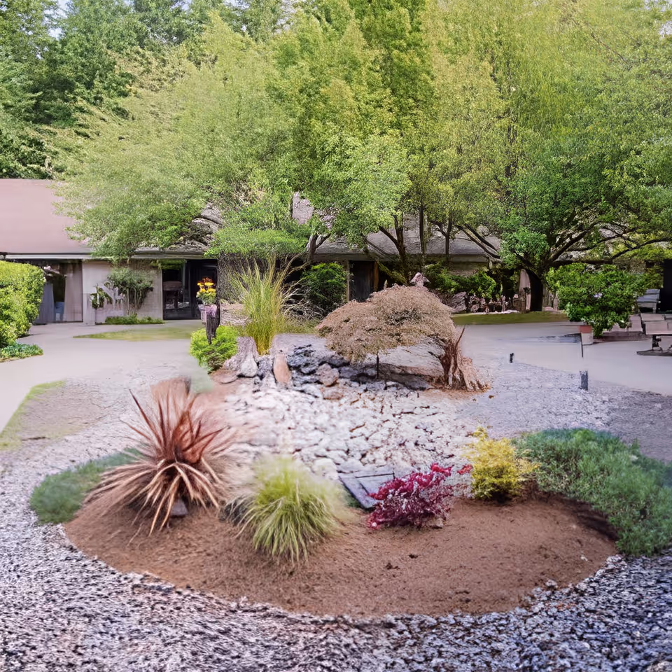 Landscaped courtyard with gravel beds, small shrubs and trees in front of a low one-story building.