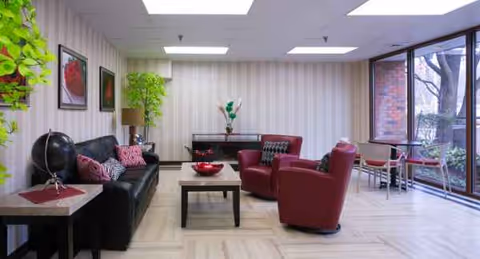 Lounge area with black sofa, red chairs, coffee table, plants, and large windows.