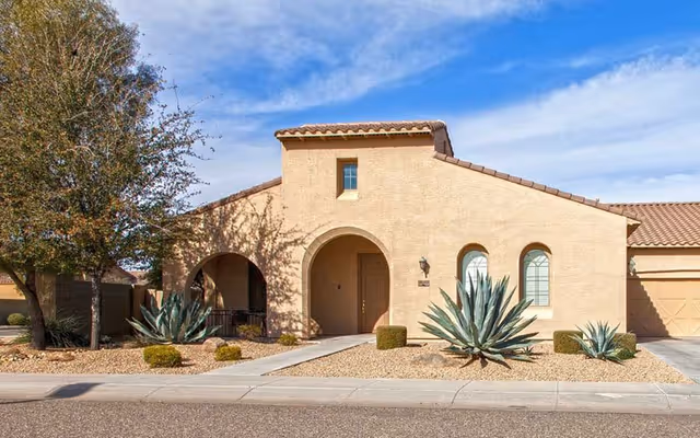 Front view of a beige stucco senior living facility with arches and desert landscaping.