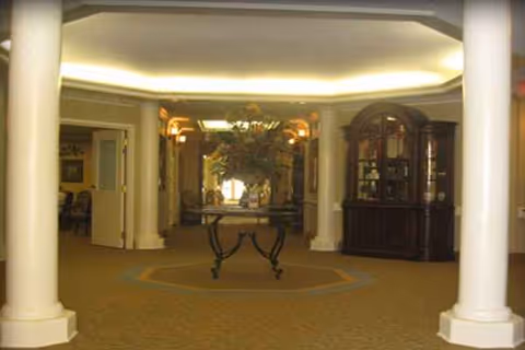 Elegant indoor lobby with columns, a central round table, and a dark wood cabinet.
