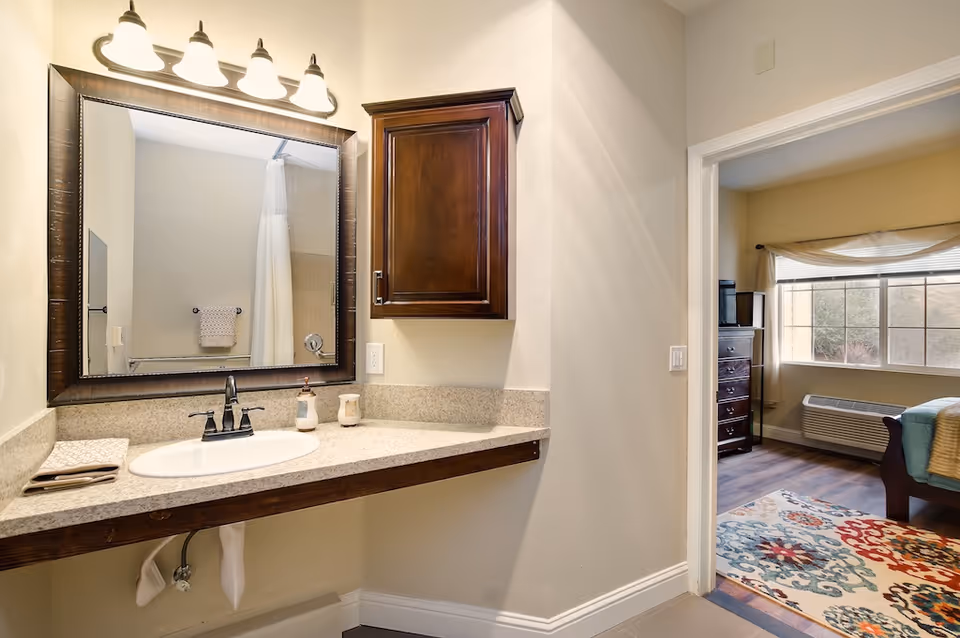 Bathroom vanity with sink, mirror, wall cabinet, and a view into an adjacent bedroom.