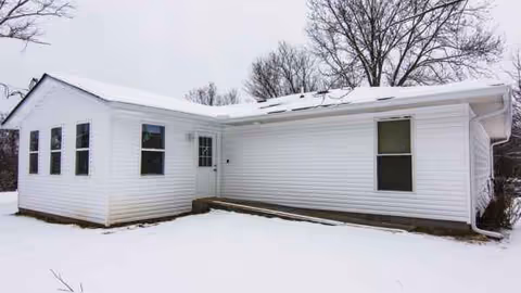 A single-story white building with multiple windows sits in a snowy landscape.