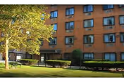 Brick senior living building with windows, trees, and a green lawn in front.