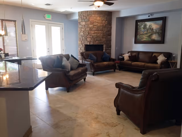 Spacious common living room with leather sofas, a stone fireplace, wall art, and a countertop at left.