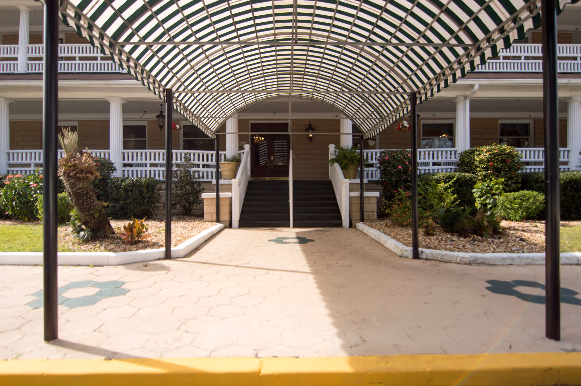 Covered entrance canopy leading to the front steps and porch of a multi-story building with white columns and landscaping.