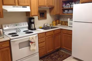 Compact kitchen with white stove, refrigerator, wooden cabinets, and sink along the counter.
