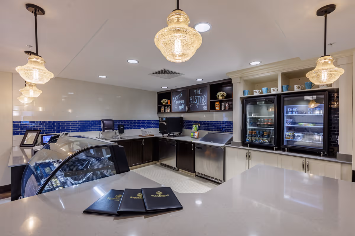 Bright bistro-style service counter with glass pendant lights, refrigerated display cases, a blue-tiled backsplash and menus on the countertop.