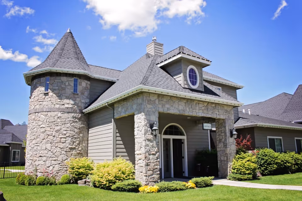 Stone-clad senior living facility building with a turret and covered entrance under a blue sky