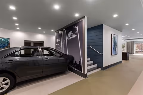 Interior lobby area with a parked car beside a staircase and large wall artwork.
