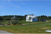 Grassy lawn with a white two-story building, a gazebo, and a parked pickup truck under a blue sky.