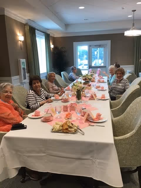 A group of elderly women seated around a long, decorated dining table in a dining room.