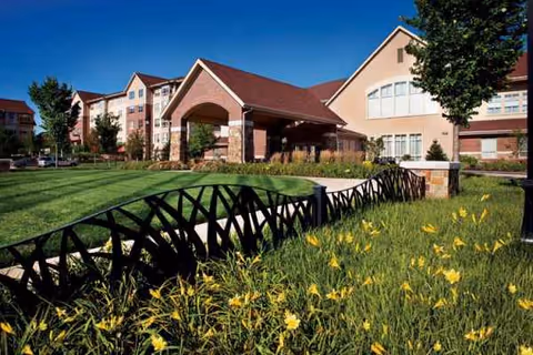 Tallgrass Creek Senior Living Community exterior with a covered entrance arch, lawns, flowering beds, and fence.