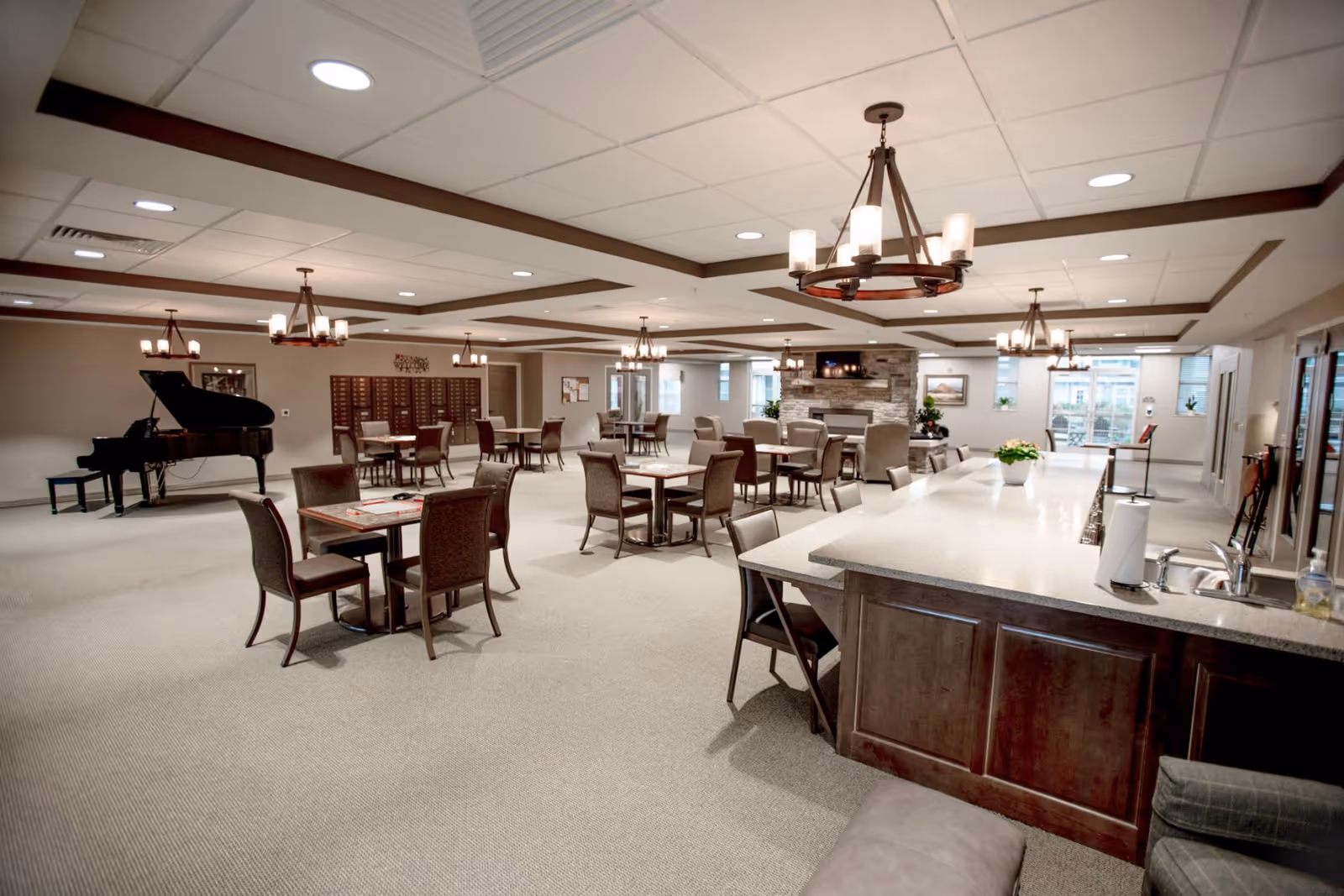 A spacious dining room featuring tables and chairs, a piano in the corner, and a cozy fireplace. The room is well-lit with chandeliers and has a modern design.