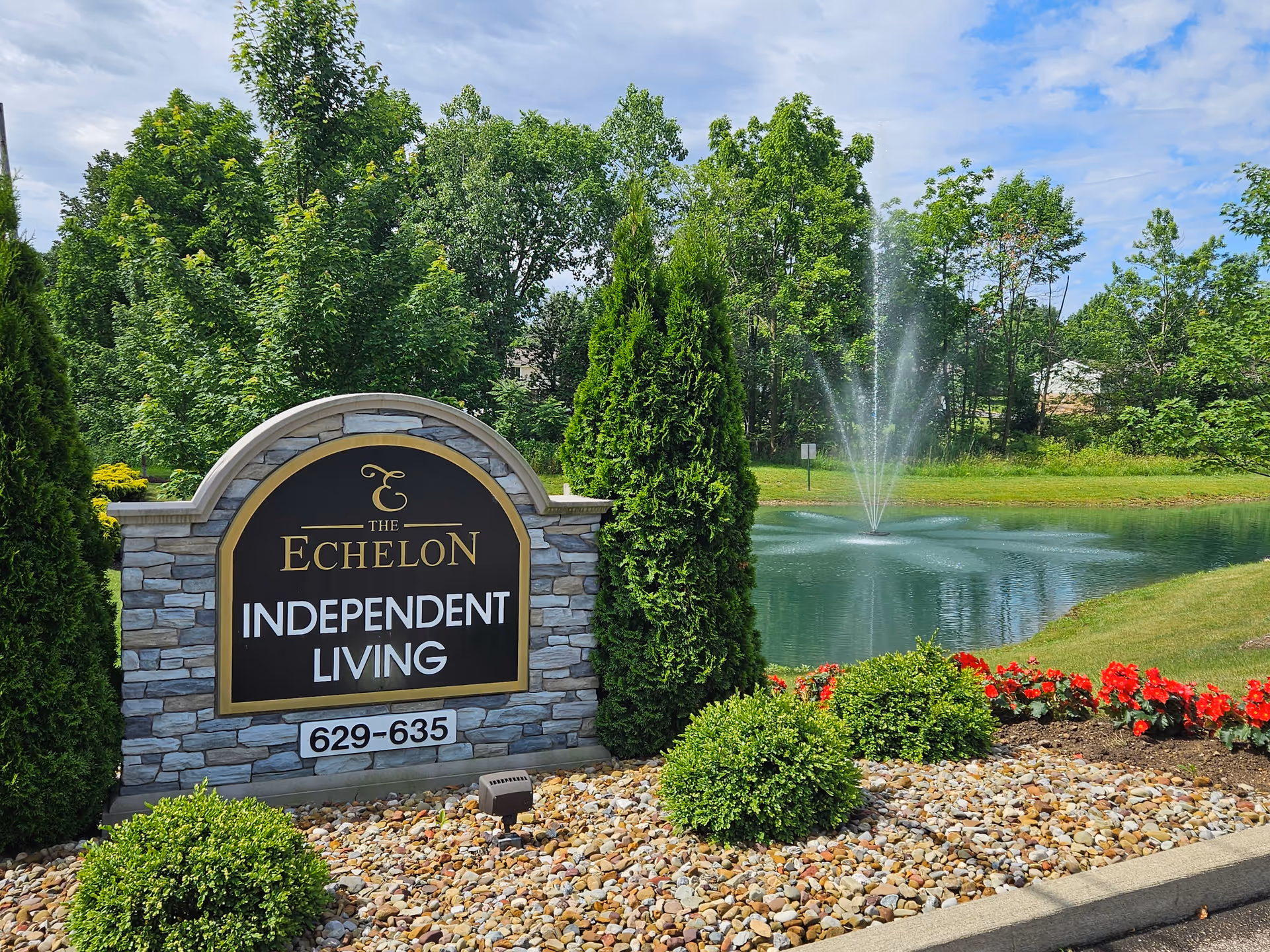 Stone entrance sign reading "The Echelon Independent Living" next to landscaped bushes and a pond with a fountain.