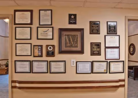 Interior wall in a senior living facility lined with numerous framed certificates and plaques.