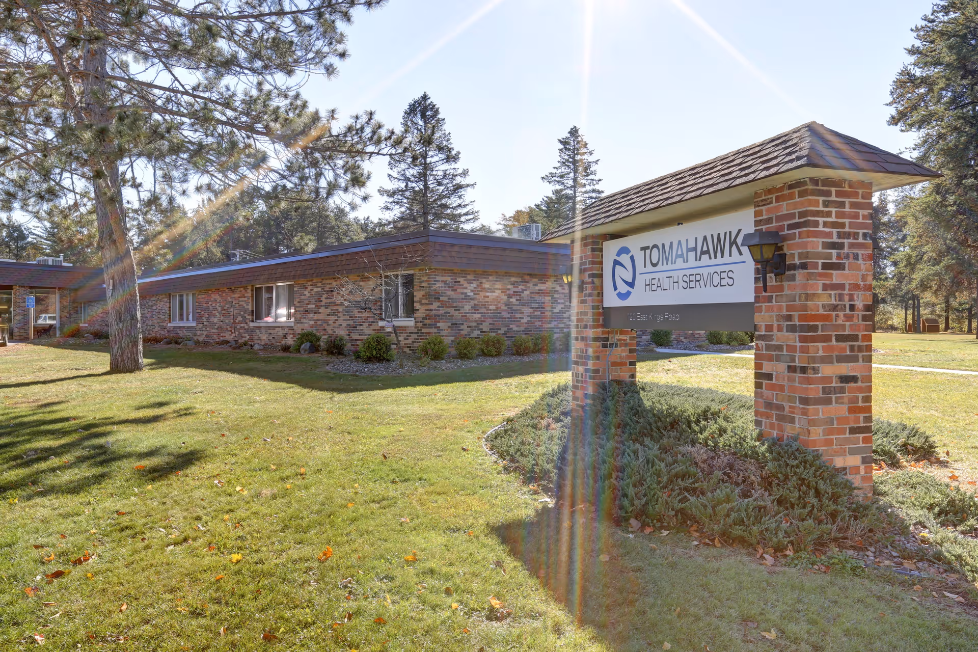 Single-story brick senior health facility with a lawn and a prominent 'Tomahawk Health Services' sign on brick pillars.