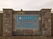 Stone-framed Journey Senior Services sign displaying the address on a cloudy day.