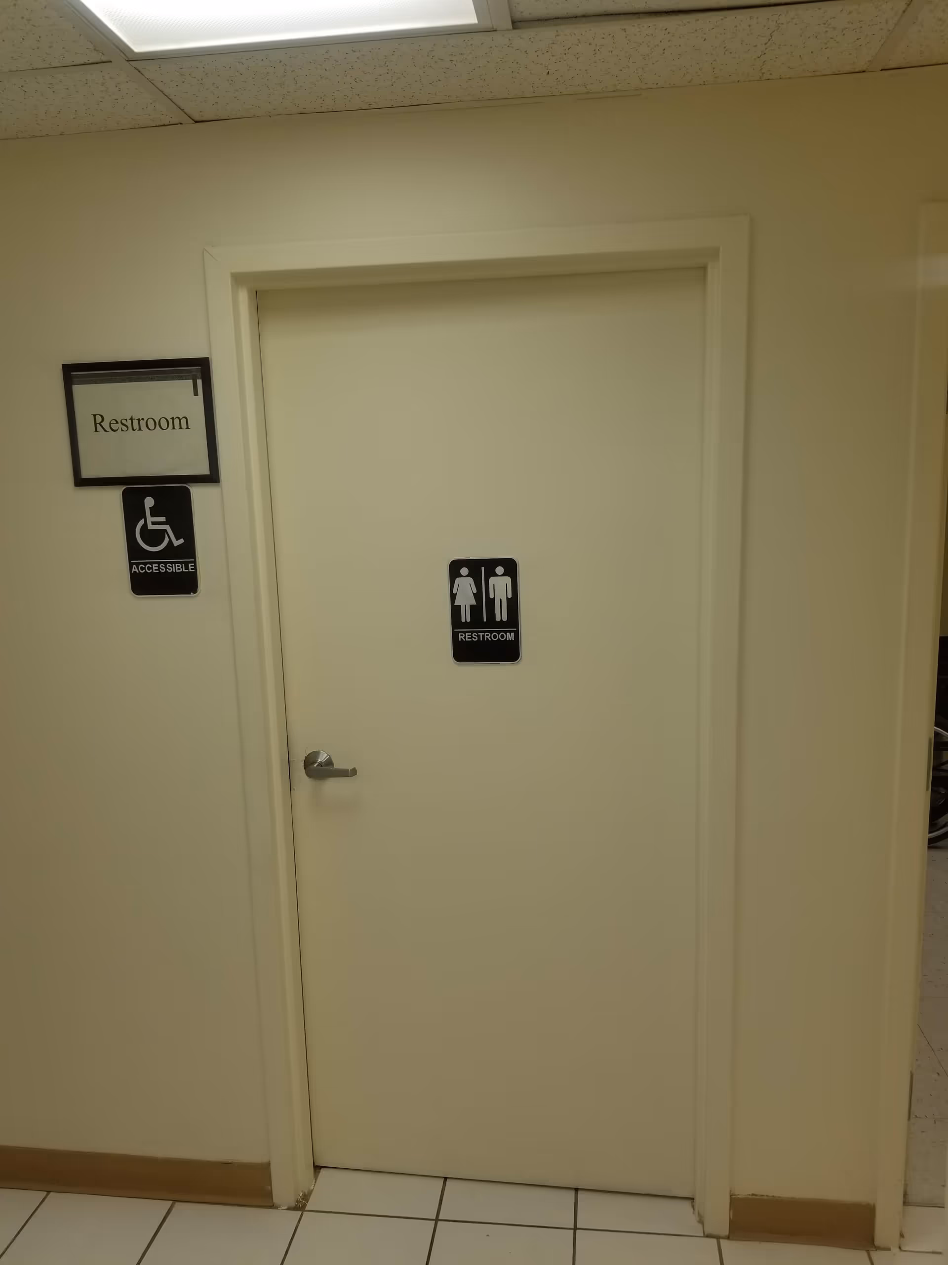Closed restroom door in a hallway with male/female and wheelchair accessible signs.