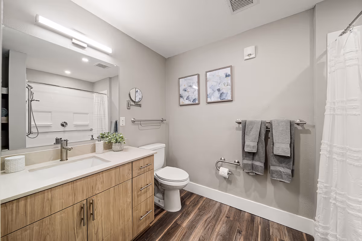 Bright modern bathroom featuring a wooden vanity with sink and mirror, a toilet, towel racks and a shower with a white curtain.