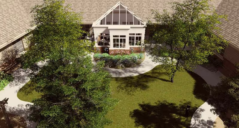 Aerial view of a courtyard garden area with green grass, trees, and a curved walking path surrounded by building walls with windows and a glass-roofed sunroom or conservatory.