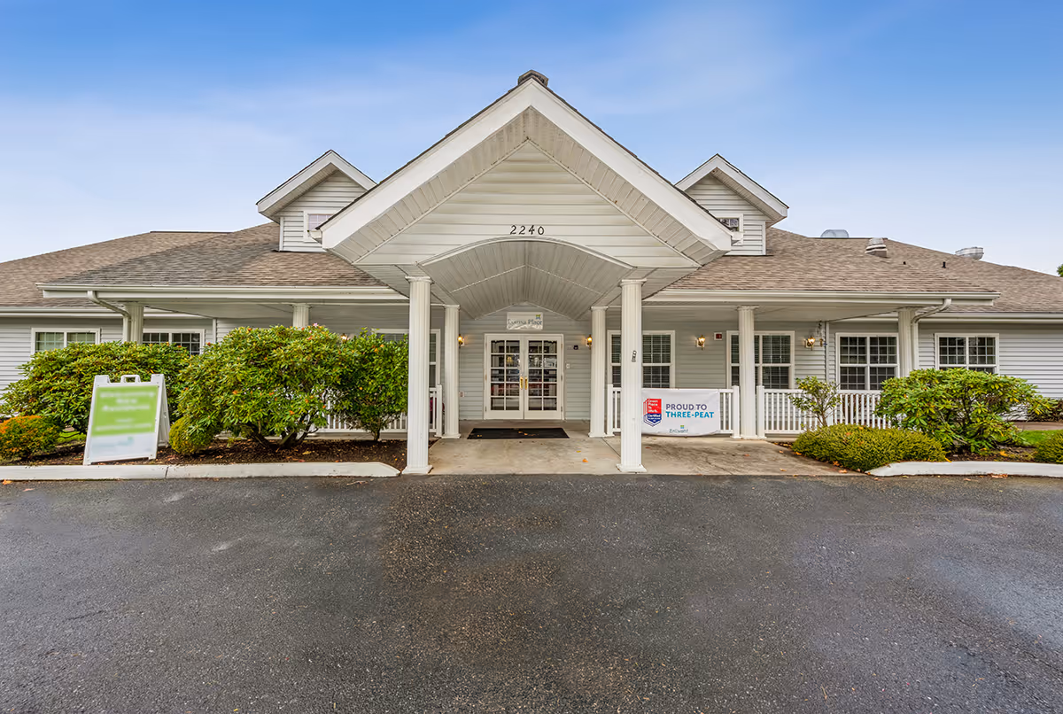 Front entrance of a single-story senior living facility with a covered portico, columns, signage, and landscaping.