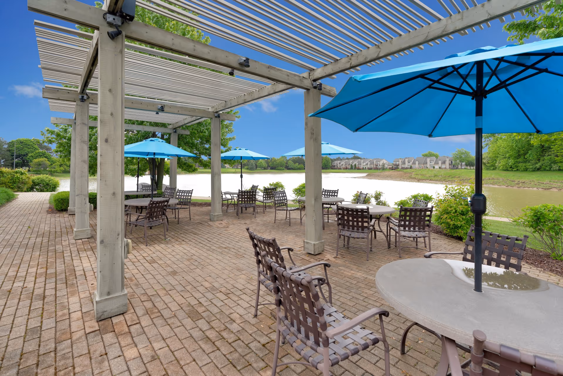 Outdoor patio with pergola, tables and blue umbrellas overlooking a lake.