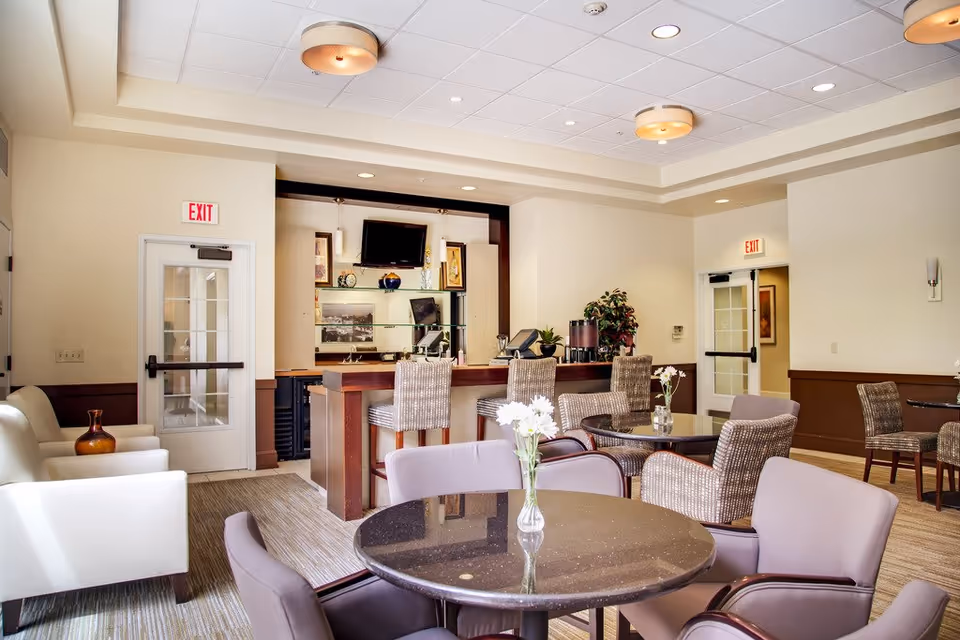 Bright communal dining and lounge area with round tables, upholstered chairs, and a service counter.