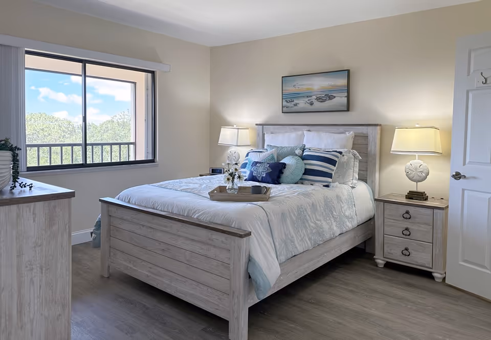 Cozy, well-lit bedroom with a bed, nightstands, lamps, and a large window view.
