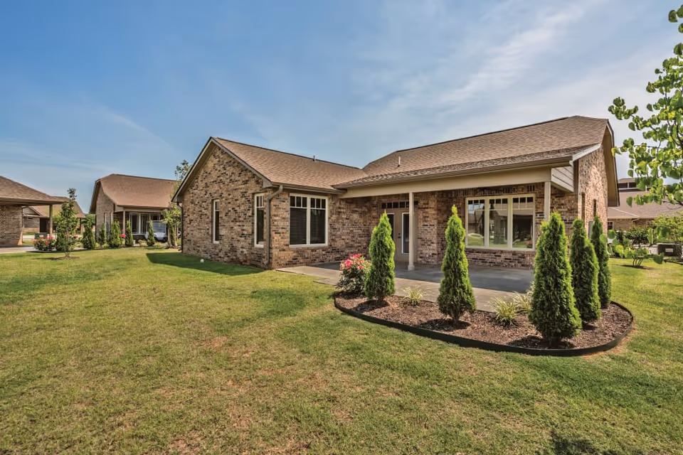 Single-story brick building with a covered front patio, manicured shrubs and a large grassy yard under a blue sky.