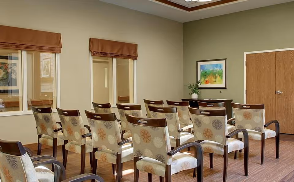 Small meeting room with rows of upholstered chairs facing a wall with artwork and double doors.