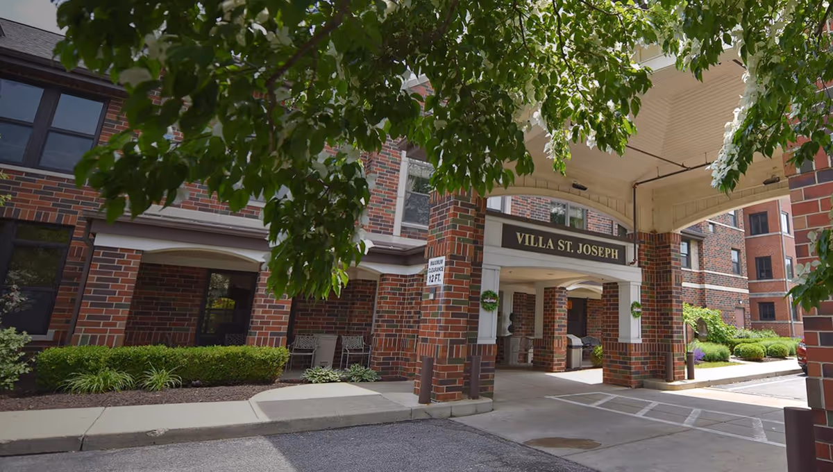 Exterior view of a brick senior-living facility entrance with a covered porte-cochère and a sign that reads VILLA ST. JOSEPH.