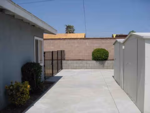 Outdoor concrete walkway at a senior living facility with a storage shed and shrubs.