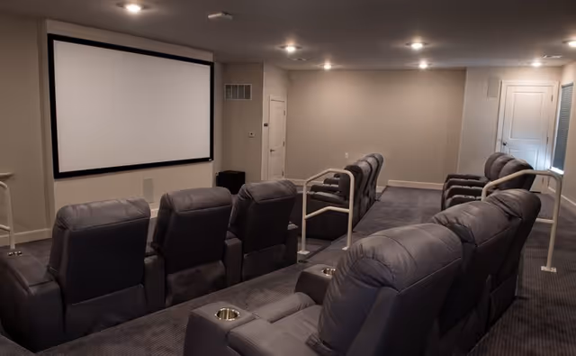 Carpeted screening room with rows of reclining leather chairs facing a large projection screen.