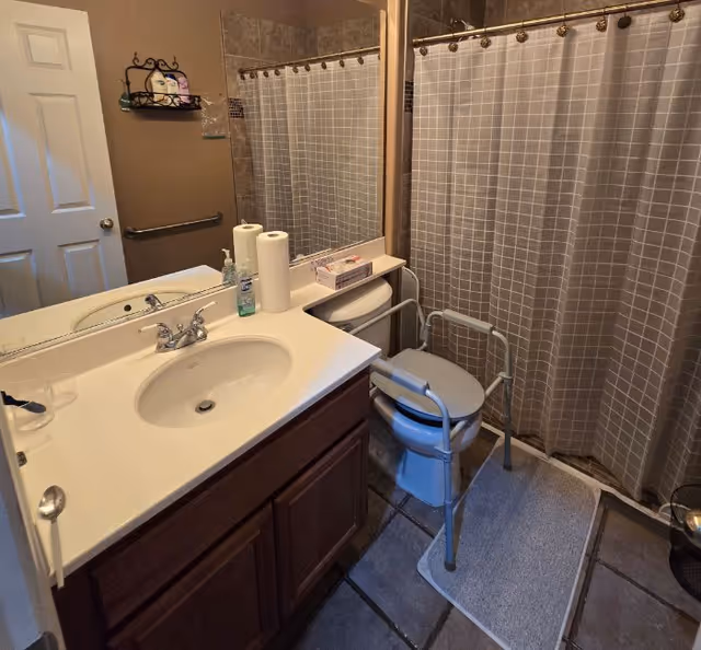 Senior living facility bathroom with sink, mirror, toilet, shower curtain, and walker.