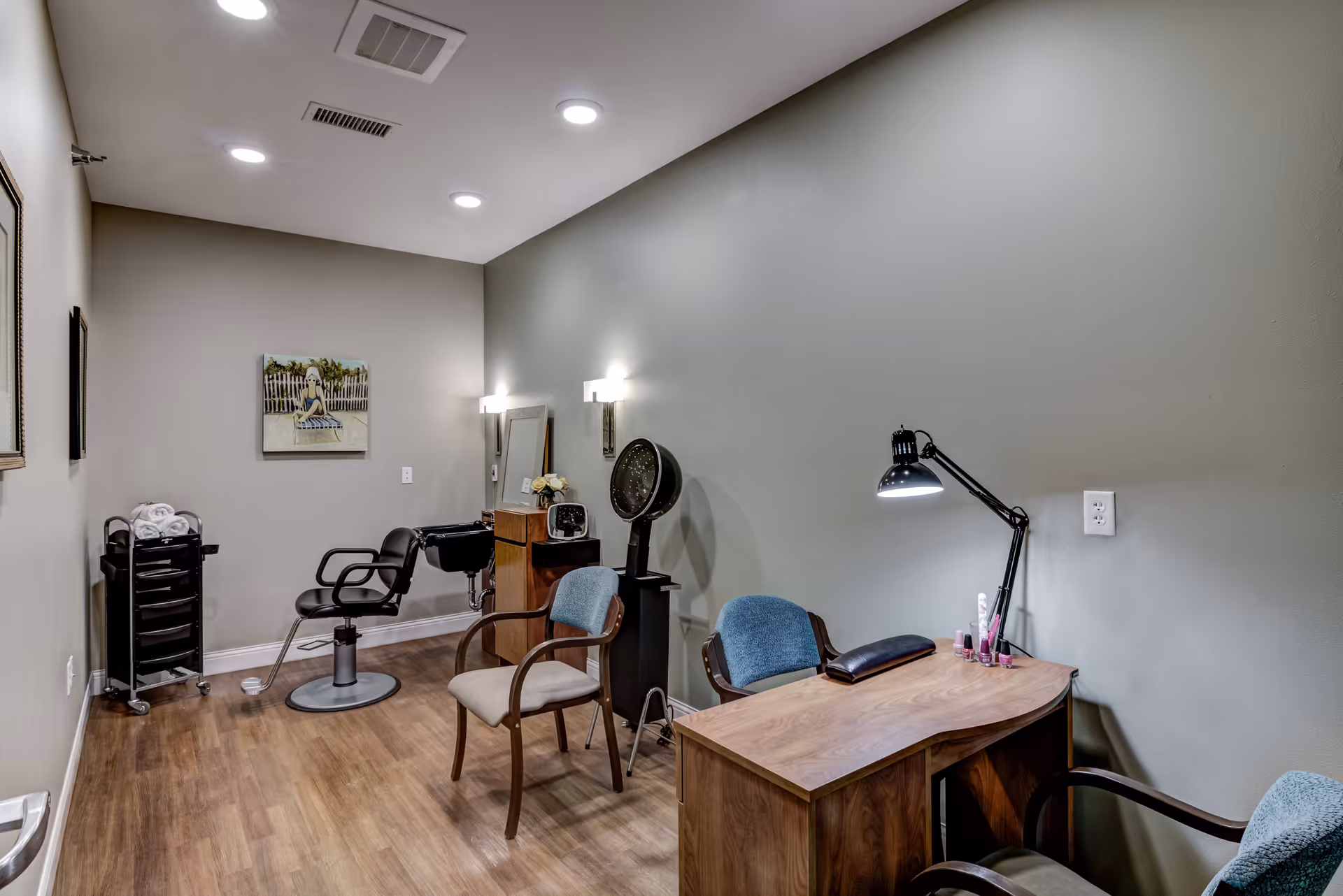 Interior salon room with a styling chair, manicure desk with lamp, hooded dryer and additional seating.