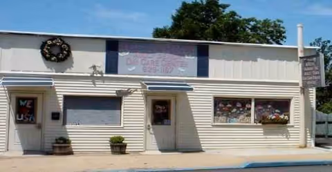 Exterior of Ageless Harmony facility with beige siding, two doors, two windows, and a wreath.