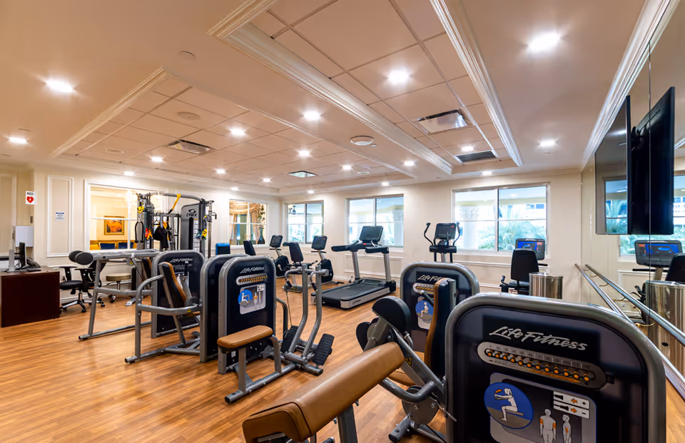 Bright, well-equipped fitness room with cardio machines and strength equipment on wood flooring.