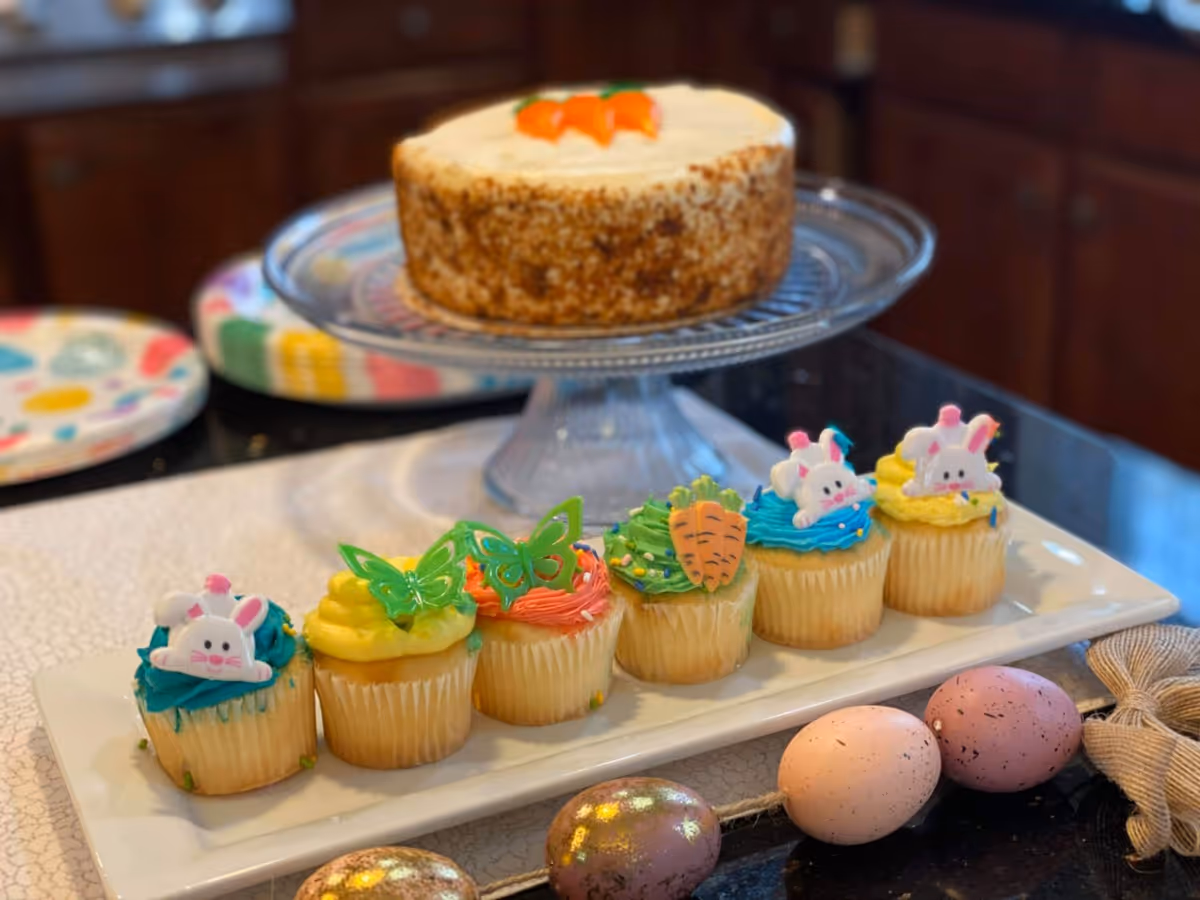 Assorted decorated cupcakes and a small cake displayed on a counter in a dining area.