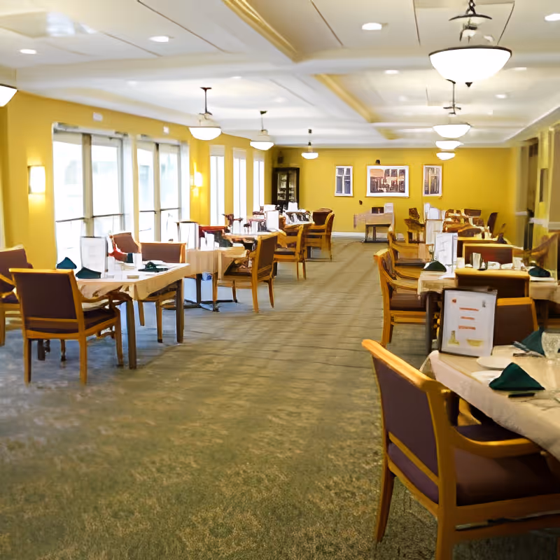 Spacious dining room with multiple set tables and chairs, yellow walls, and ceiling lights.
