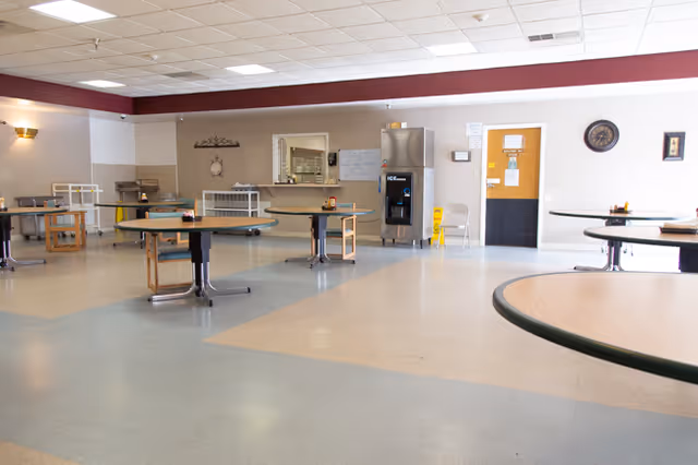Spacious, empty dining room with round tables, a service counter and a beverage/ice machine along the far wall.