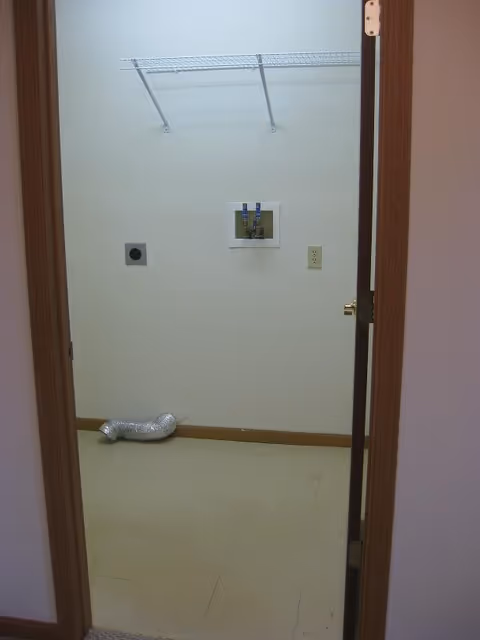 Empty laundry/utility room with washer/dryer hookups, a wall shelf, and a vent hose on the floor.