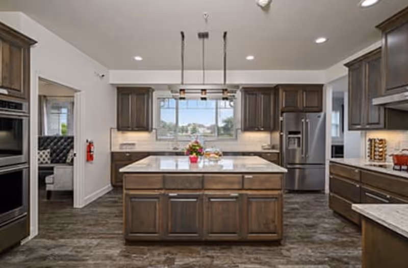 Bright modern kitchen with a large central island, dark wood cabinets, stainless steel appliances, and pendant lights.