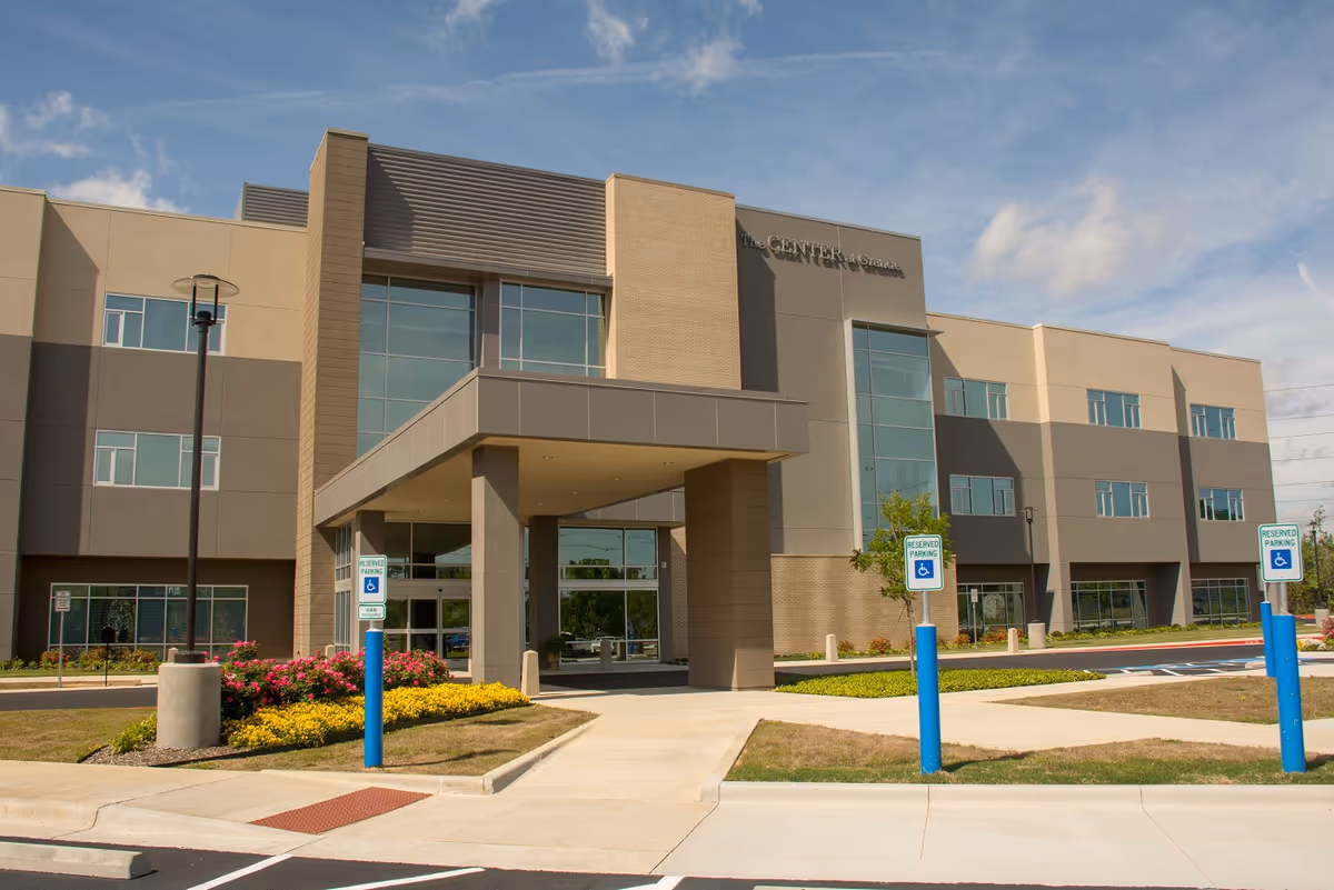 Front exterior of a modern three-story building with a covered entrance, landscaping, and accessible parking signs.