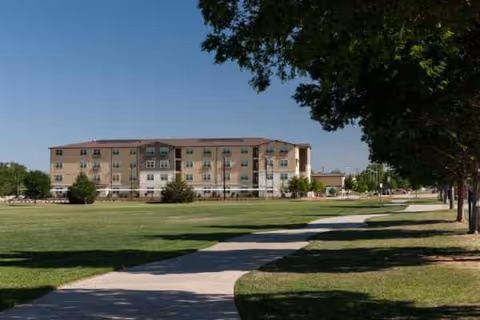A multi-story senior living facility with a green lawn, trees, and a curved walkway.