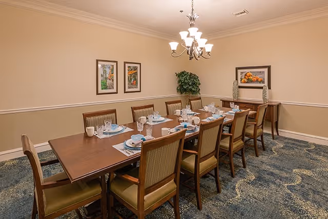 A formal dining room with a long table set for ten, upholstered chairs, chandelier lighting, framed artwork, and a sideboard.