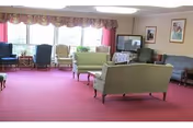 Communal living room with sofas and armchairs arranged around large windows and a television.