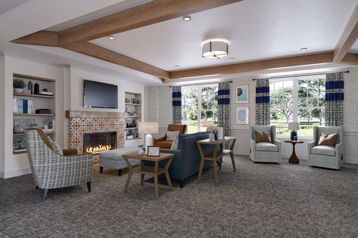 A cozy living room with a fireplace featuring decorative tiles, a mounted flat-screen TV above it, and built-in shelves on either side. The room has a patterned carpet, wooden ceiling beams, and large windows with patterned curtains letting in natural light. There are multiple seating options including armchairs, a sofa, and side tables with lamps and decorative items.