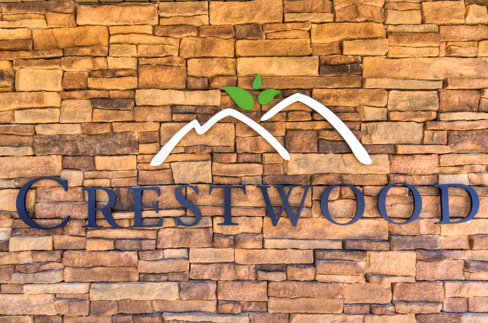 Sign on a stone wall displaying the name Crestwood with a logo of two white mountain peaks and three green leaves above the text.