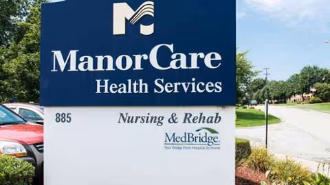 Large blue ManorCare Health Services sign outside the nursing and rehabilitation center.