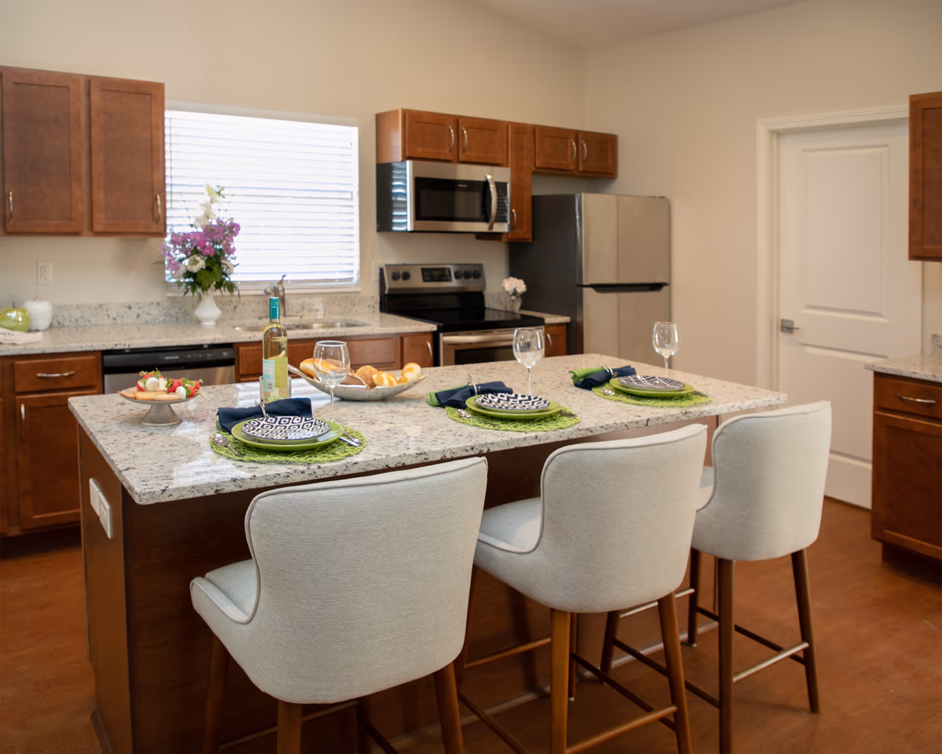Bright modern kitchen with a granite island set for three and three upholstered bar stools.